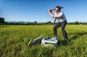 Man in tie smashes printer with baseball bat in a field. 