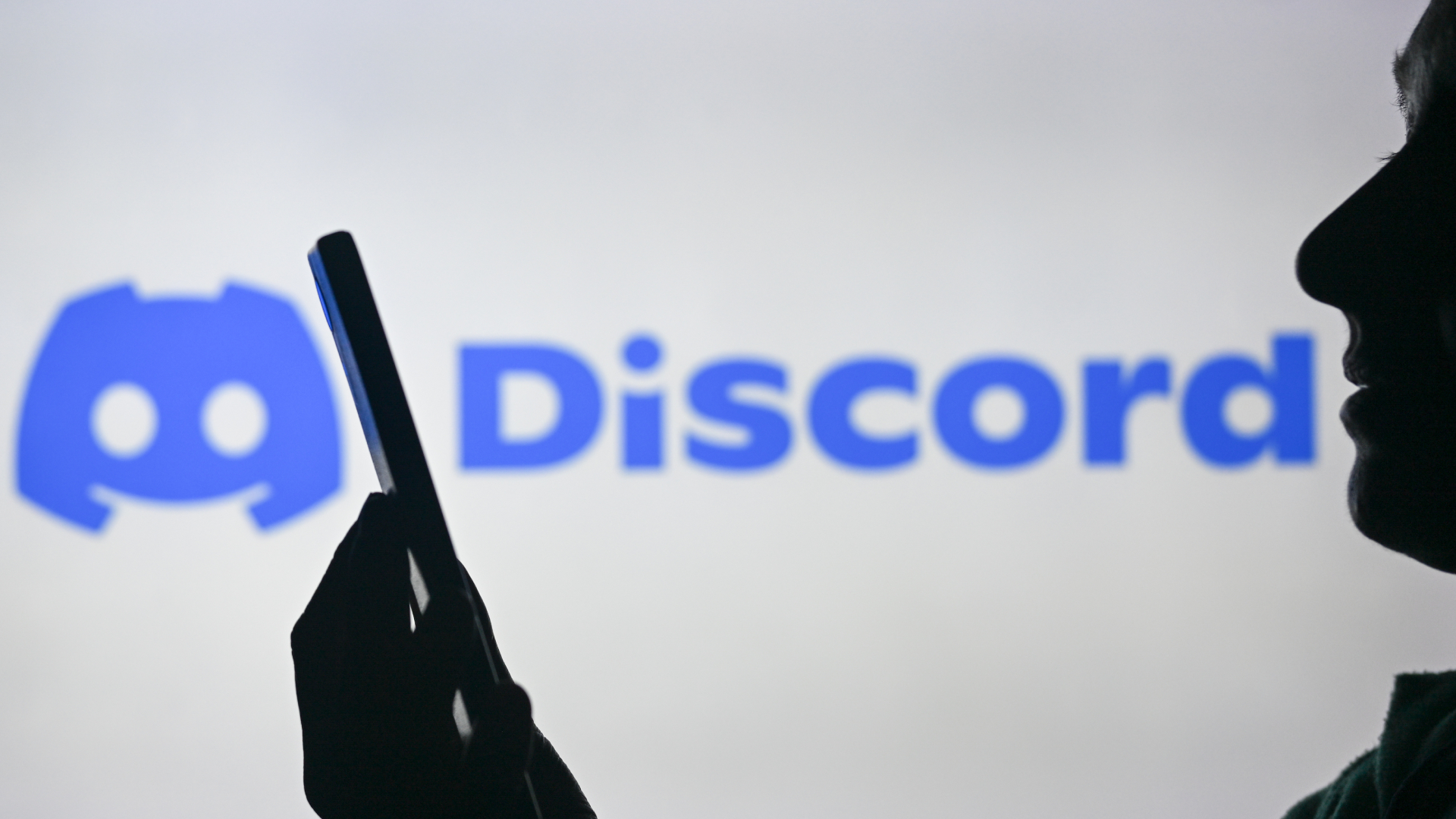 EDMONTON, CANADA - APRIL 28: An image of a woman holding a cell phone in front of the Discord logo displayed on a computer screen, on April 29, 2024, in Edmonton, Canada.